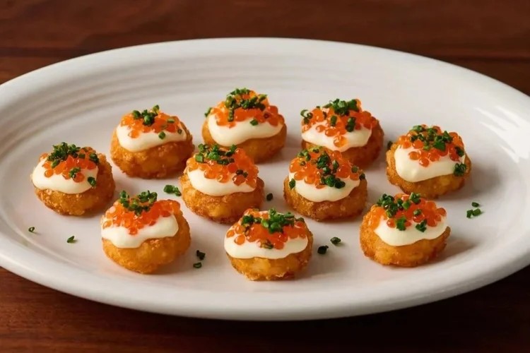 Ten bite-sized appetizers with a crispy base, topped with a dollop of cream, orange fish roe, and sprinkled with chopped herbs, arranged neatly on a white plate.