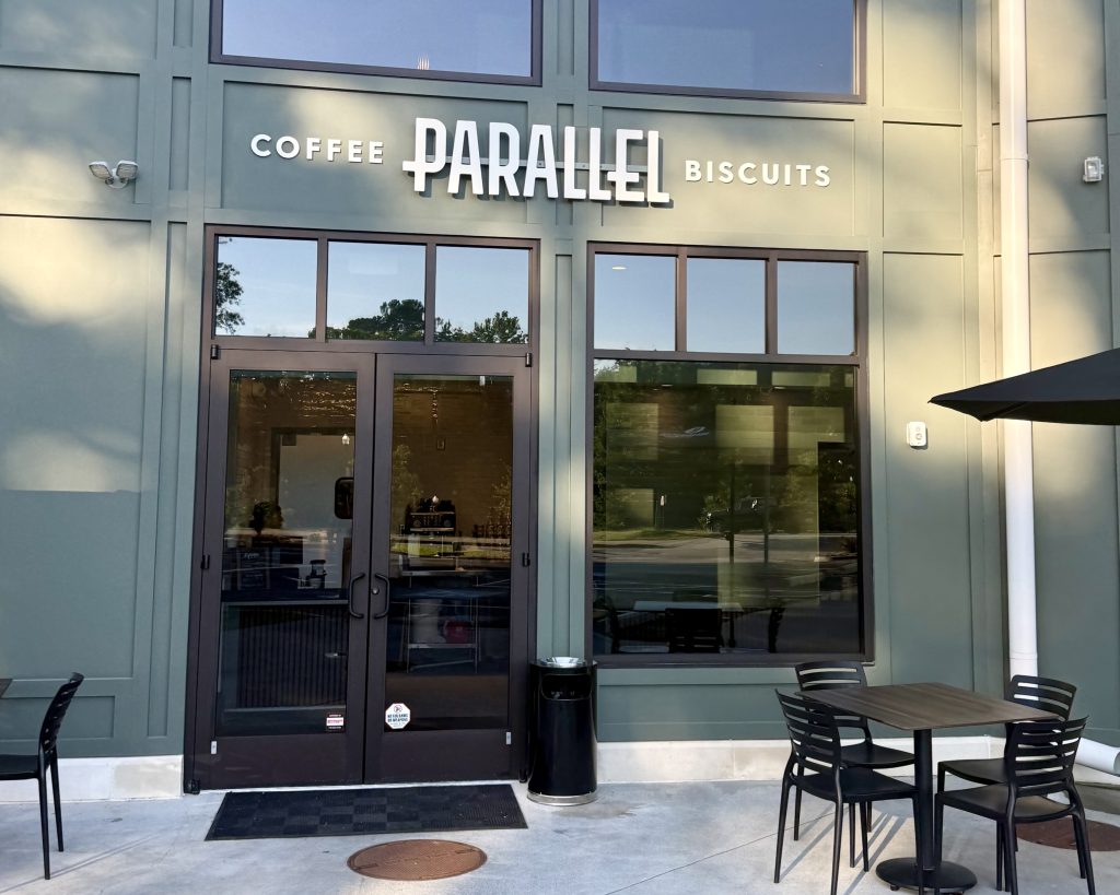 The exterior of Parallel, a café offering coffee and biscuits, with glass doors, windows, and outdoor seating with black chairs and tables.