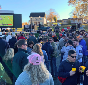A crowd gathers outdoors in Acworth this fall to watch a Tennessee Volunteers football game on a large screen set up in a parking lot.