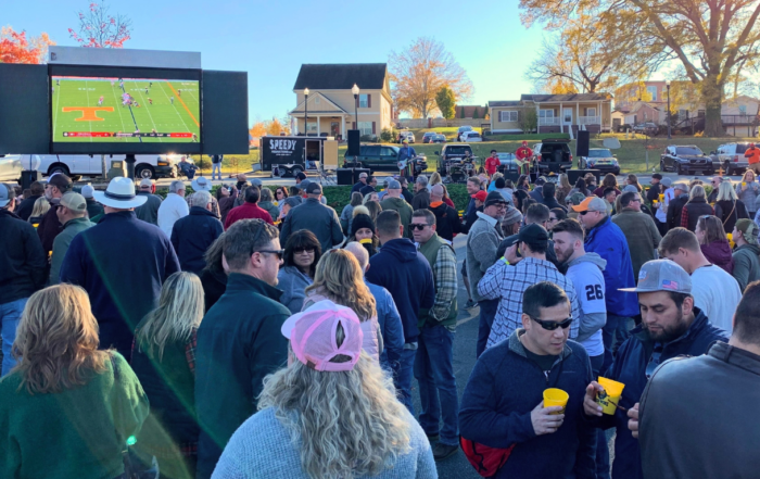 A crowd gathers outdoors in Acworth this fall to watch a Tennessee Volunteers football game on a large screen set up in a parking lot.