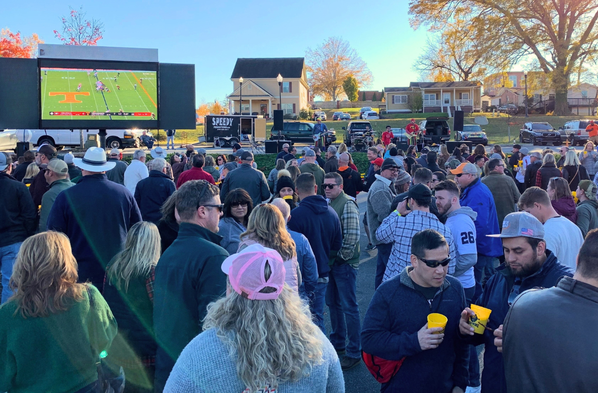 A crowd gathers outdoors in Acworth this fall to watch a Tennessee Volunteers football game on a large screen set up in a parking lot.