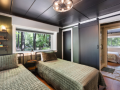 A bedroom with two twin beds featuring quilted olive green bedspreads, a window overlooking trees, and a sliding barn door leading to an ensuite bathroom.