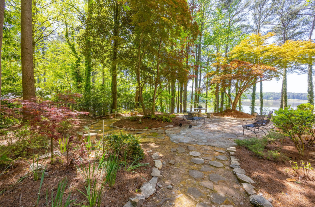 A flagstone path leads through a wooded backyard to a patio overlooking a lake.