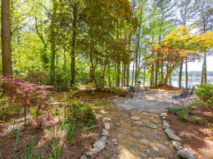 A flagstone path leads through a wooded backyard to a patio overlooking a lake.