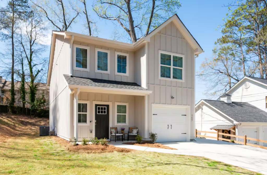 Two-story light gray house with board and batten siding, a dark front door, and a single-car garage.