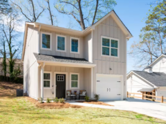 Two-story light gray house with board and batten siding, a dark front door, and a single-car garage.
