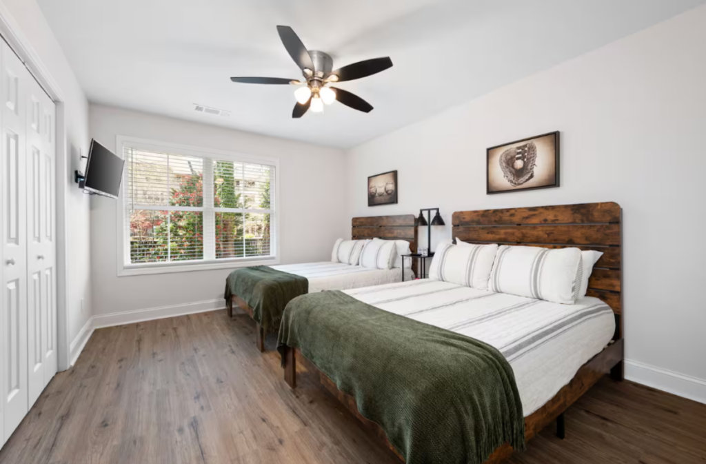 Bedroom with two queen beds featuring wooden headboards, white striped bedding, and green throws.