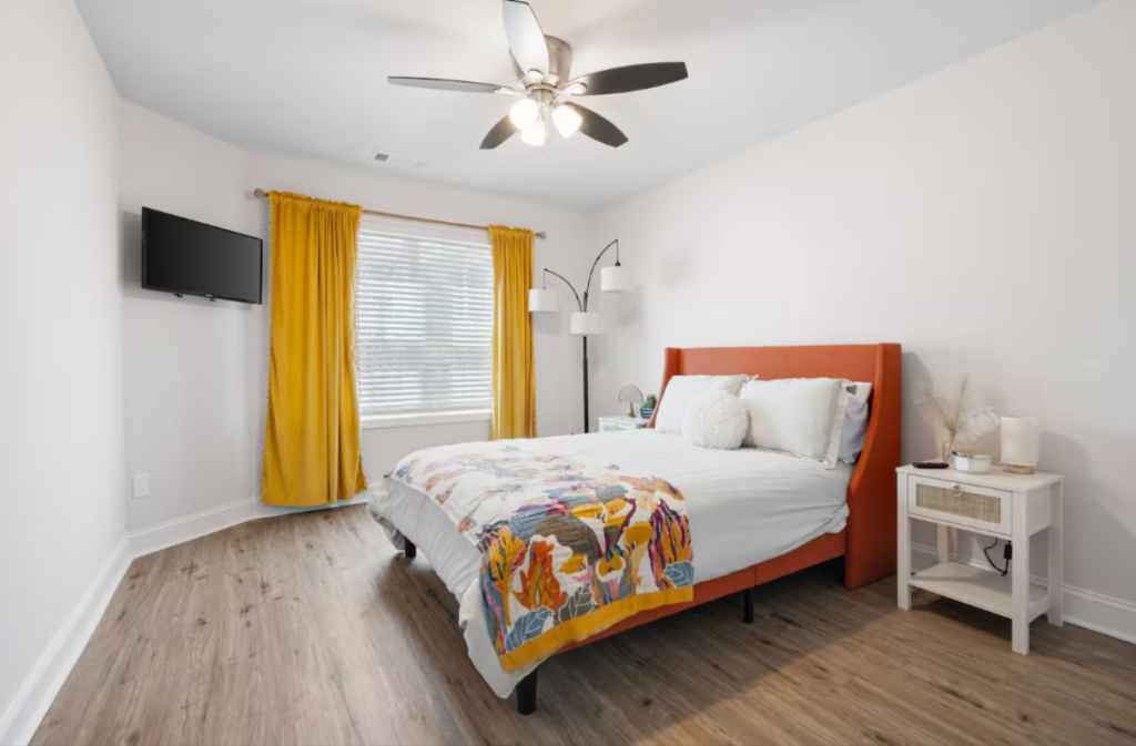 Bedroom with an orange upholstered bed, bright yellow curtains, and a white nightstand.