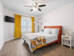 Bedroom with an orange upholstered bed, bright yellow curtains, and a white nightstand.