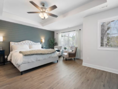 Bedroom with a tufted white bed, an accent wall with gray horizontal paneling, and two armchairs by a window.