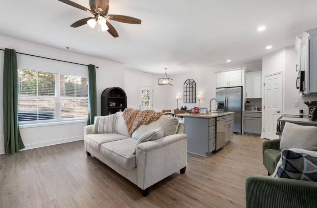 Open-concept living room and kitchen with a beige sofa, kitchen island, and hardwood floors.